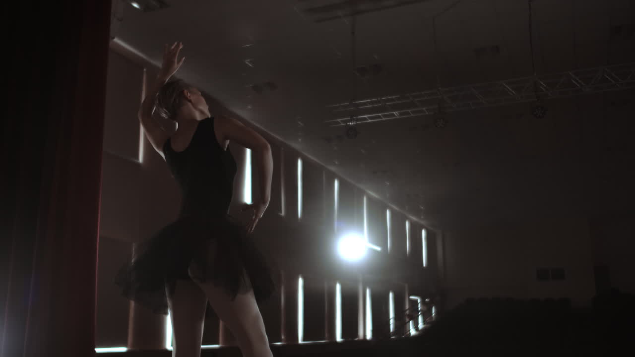 Slow motion: Diligent young graceful ballerina dancing elements of classical ballet in the dark with light and smoke on the background. Beautiful young ballerina in darkness.