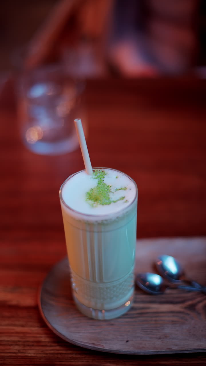 Bir kafede masanın üzerinde pipetli bir bardakta matcha latte yakın çekim. Dikey