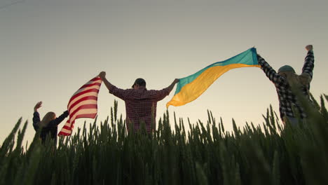 un grupo de amigos levanta la bandera de los estados unidos y la bandera de ucrania sobre sus cabezas.