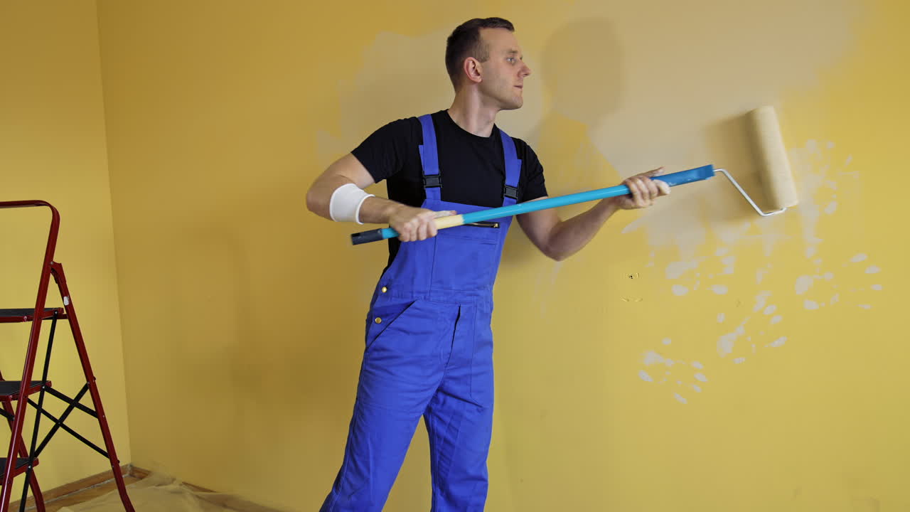 Man paints wall with roller. Painter man at work painting wall with roller