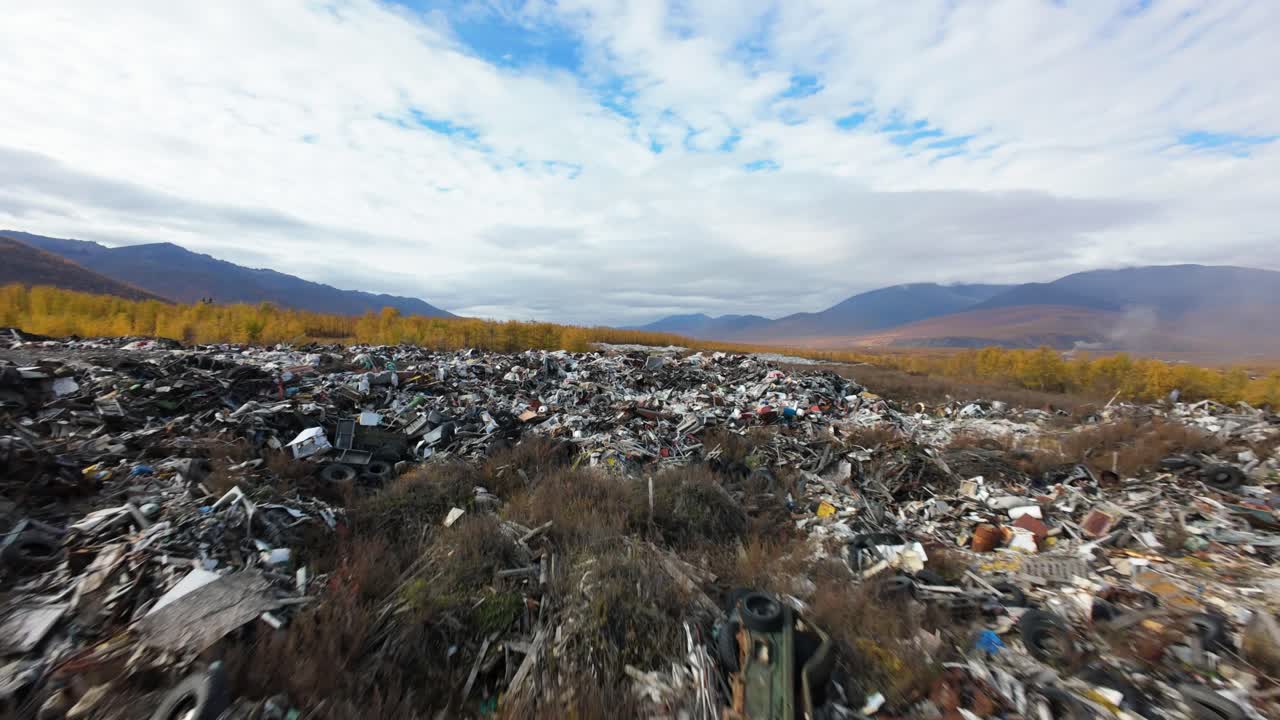 A stark view of a sprawling household waste dump reveals a troubling reality in nature’s embrace. The contrast of vibrant autumn colors juxtaposes with discarded debris under a clouded sky.