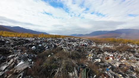 a stark view of a sprawling household waste dump reveals a troubling reality in nature’s embrace. the contrast of vibrant autumn colors juxtaposes with discarded debris under a clouded sky.