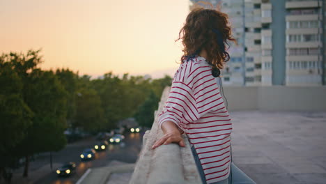 chica de la ciudad posando puesta de sol en el techo. mujer despreocupada apoyándose en las barandillas por la noche
