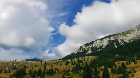 Lapso-De-Tiempo-De-Nubes-Pasando-Sobre-Un-Prado,-Un-Bosque-De-Pinos-Y-Un-Acantilado-De-Montaña