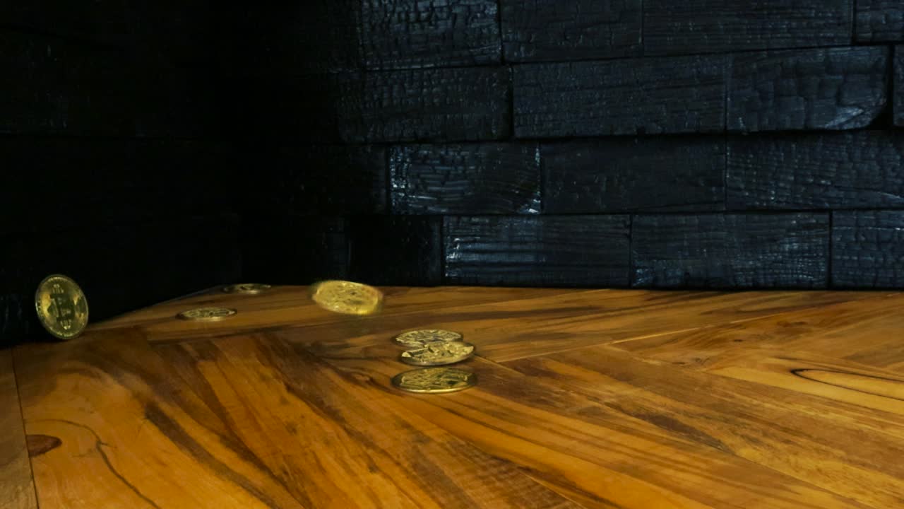 Gorgeous slow motion footage of golden and shiny Bitcoin cryptocurrency money coins fallin on an olive wood brown and yellow table with yakisugi burned wall panels in the background. Bouncing coins