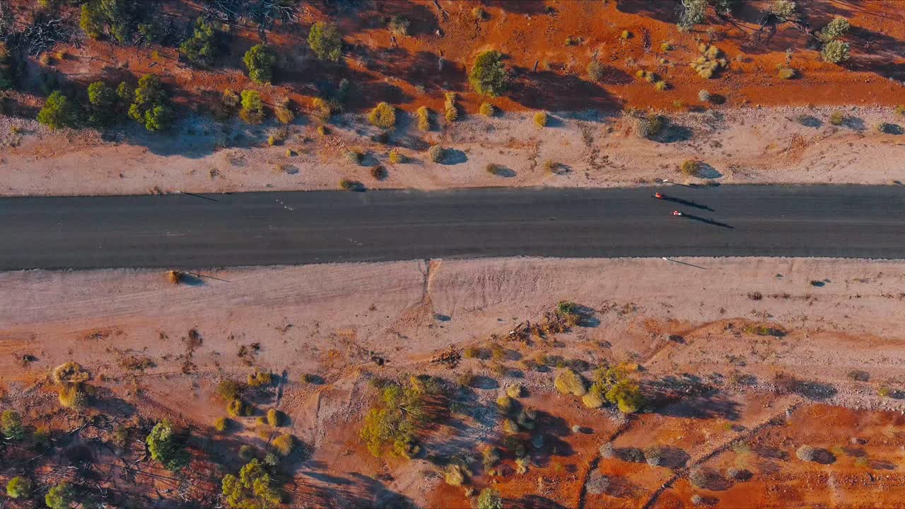 Aerial view of two cyclists riding on an outback remote outback road with orange dirt and dusty sand lining the roadside