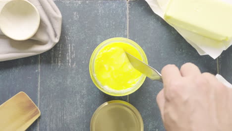 man's hand takes creamy butter ghee from a pot with butter knife