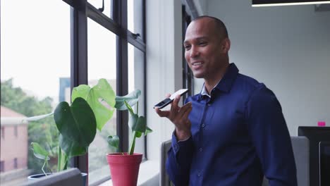 Mixed-race-businessman-standing-talking-on-smartphone-looking-out-of-window-in-office