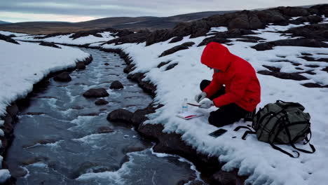 person studying a stream in snowy mountain landscape
