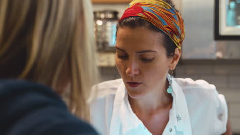 Mujer-Joven-Hablando-Con-Un-Cliente-En-El-Mostrador-De-Una-Tienda-De-Delicatessen