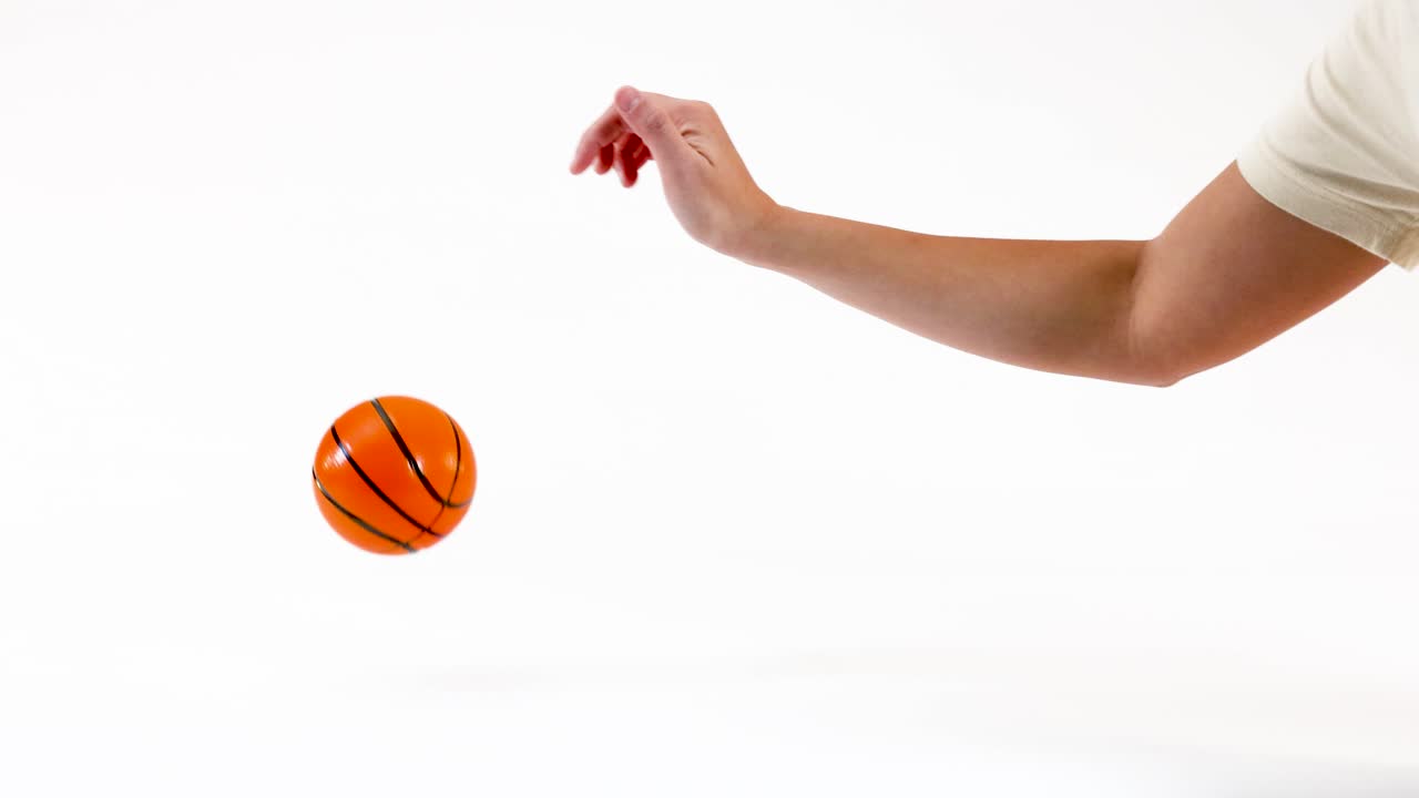 A person's hand drops a small toy basketball which bounces and rolls across white space
