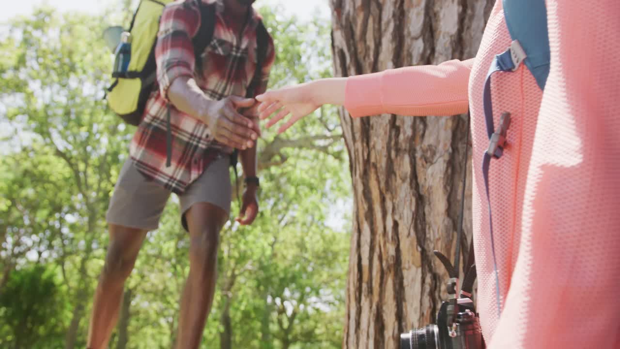 pareja diversa caminando con mochilas y tomados de la mano en el parque, cámara lenta
