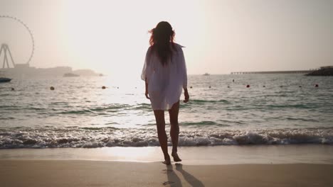 woman in a white shirt walks along the beach of the persian gulf in dubai