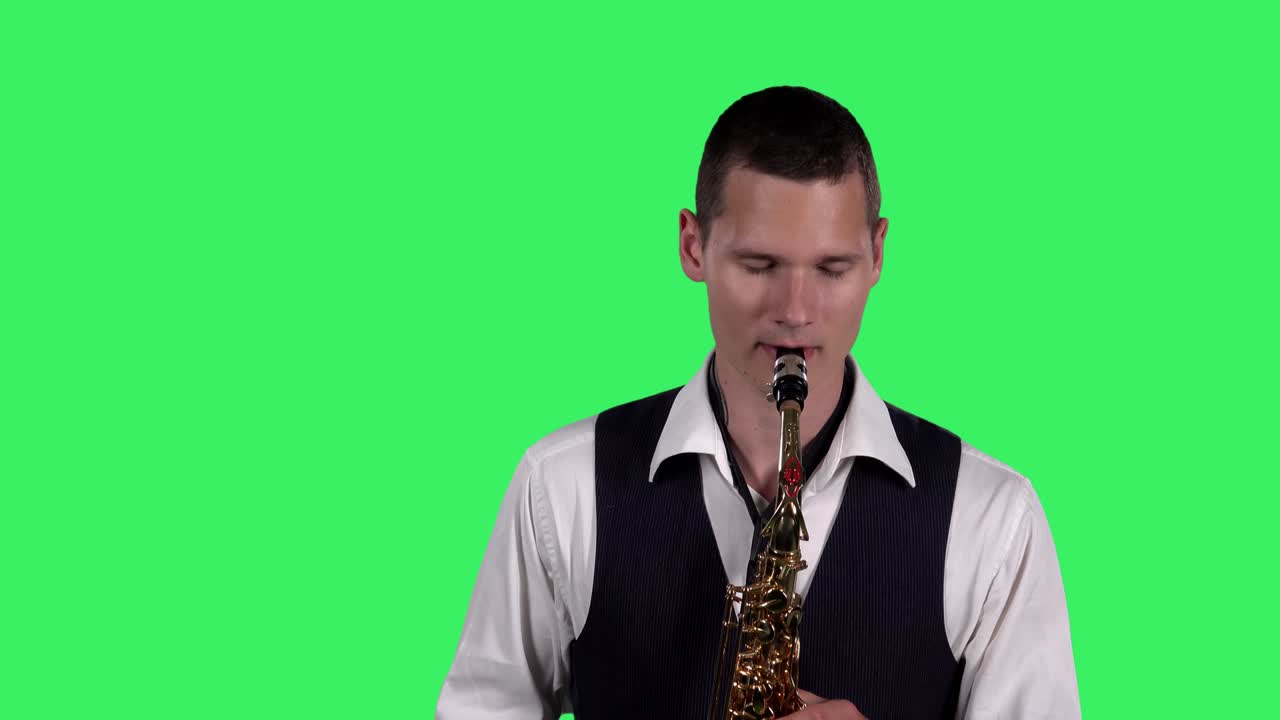 초상화: 스타일리시한 젊은이가 스튜디오에서 녹색 스크린에서 색소폰으로 느린 멜로디를 연주합니다. 색소폰 연주자가 솔로를 연주하고 있습니다.