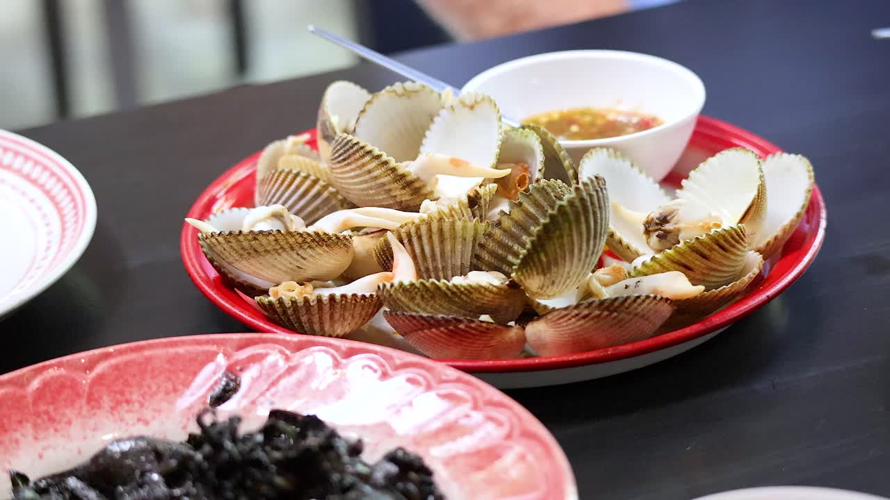 Person enjoying boiled clams with dipping sauce in Phuket, Thailand