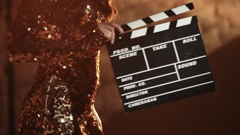 woman in golden sequins dress holding clapperboard