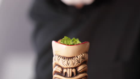 Bartender-Adding-Mint-Leaves-To-Cocktail-Drink-In-Wooden-Tiki---extreme-close-up