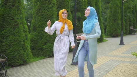 two positive expressive attractive muslim young woman in traditional scarf dancing in the park