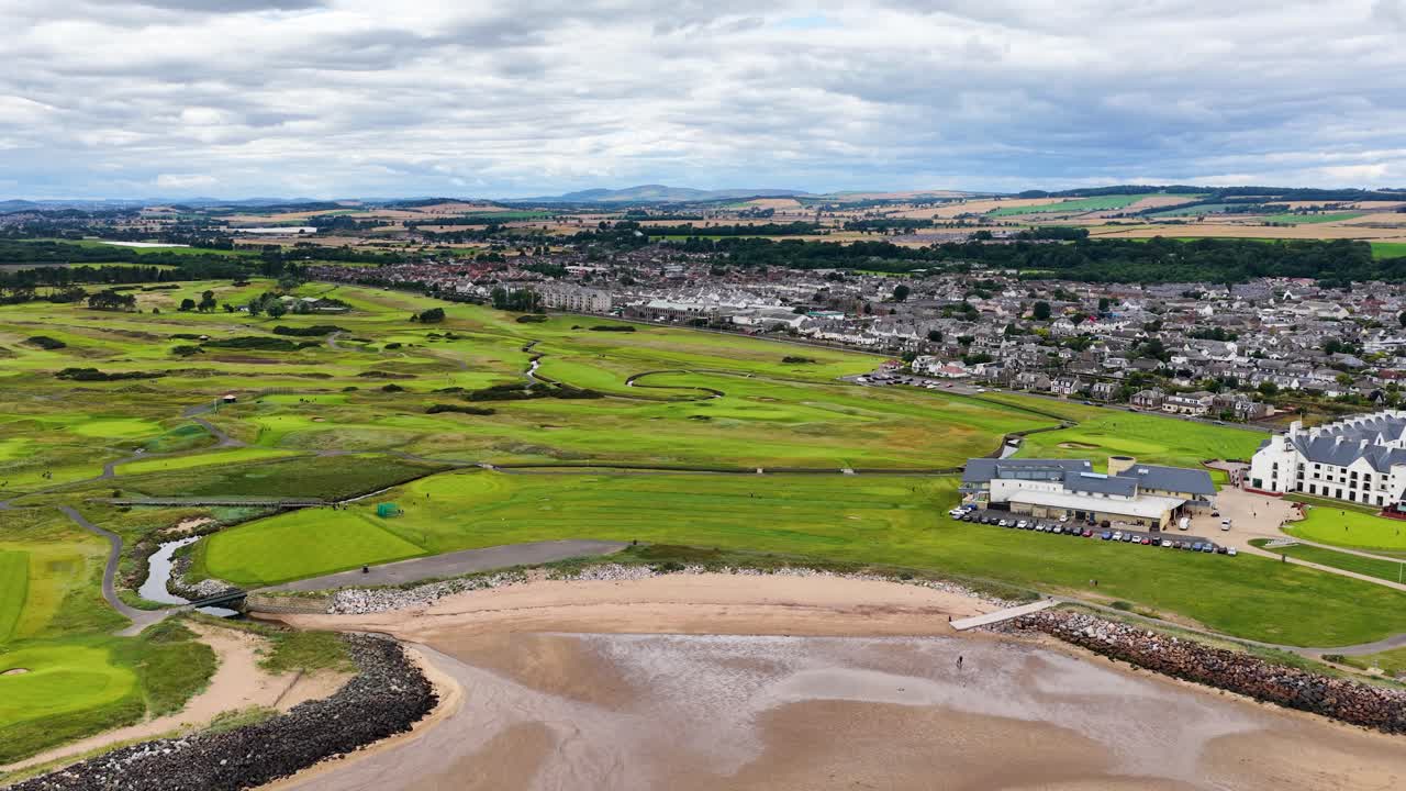Drone pans above Carnoustie golf course, fairways, bunkers, coastline, under overcast daylight