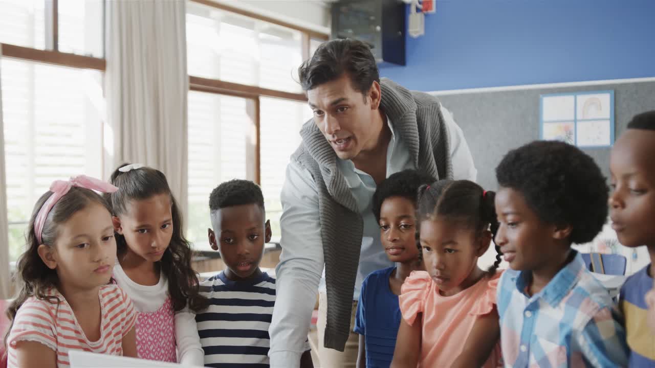 diverso maestro masculino feliz y niños usando computadora portátil en clase de escuela primaria, cámara lenta