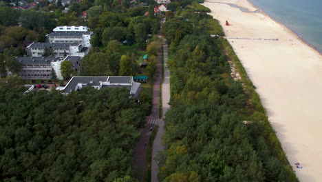 Toma-Aérea-De-Arriba-Hacia-Abajo-De-Una-Playa-De-Arena-Con-Bosque-Verde-Y-Camino-En-Gdansk,-Polonia