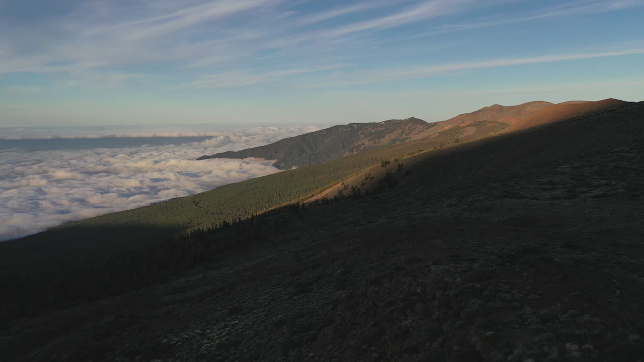 Three people standing on a cliff below the Pico de Teide mountain looking out on the hillside and a heavy cloud inversion in the valley in the evening. Backpacking below Pico de Teide at sunset 4k.