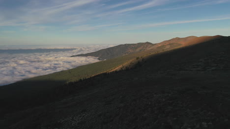 three people standing on a cliff below the pico de teide mountain looking out on the hillside and a heavy cloud inversion in the valley in the evening. backpacking below pico de teide at sunset 4k.