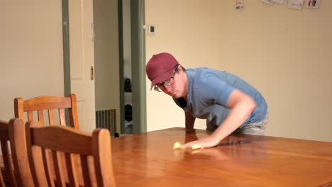 man sprays and wipes a large wooden kitchen family table