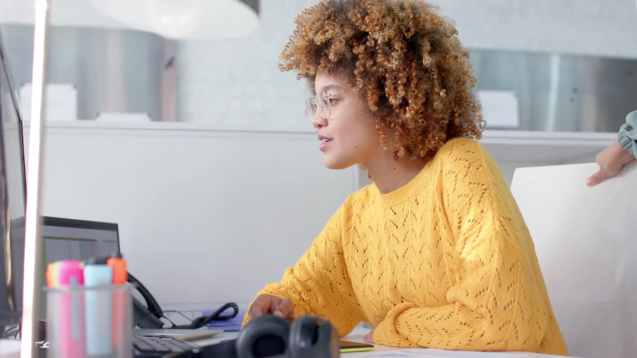 Happy diverse female colleagues using computer and discussing work at desk, slow motion