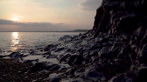 Gezeiten-überspülen-Pebble-Beach-Am-Fuße-Der-Felsen-Bei-Sonnenuntergang,-Ogmore-On-Sea,-Südwales,-Großbritannien