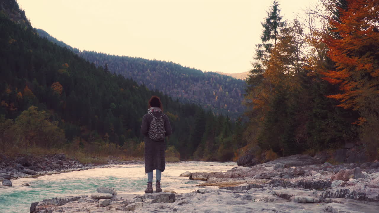 Cinemagraph of young woman hiker at a river in German Alps with autumn forest and motion in water