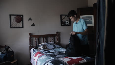 young man, high school aged teenage boy packs his backpack in his bedroom