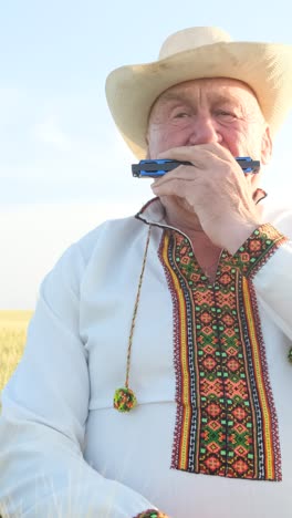 a lonely talented elderly man in ukrainian national clothes plays the harmonica a lonely talented elderly man in ukrainian national clothes plays the mouth organ harmonica sits in the middle of the field grandfather in an embroidered shirt
