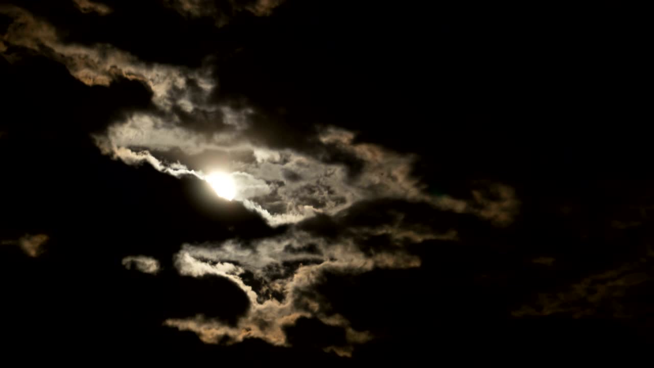 보름달은 밤하늘에서 어두운 구름과 나무를 가로질러 움직인다.