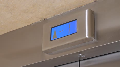 blue screen with arrow on metal panel shows lifting up of contemporary elevator in highrise building close low angle shot.