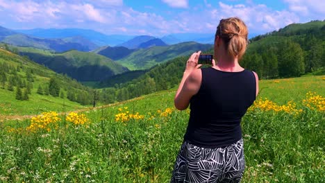 Capturing Nature&#039;s Beauty: A Woman Photographing Breathtaking Mountain Scenery in a Lush Green Landscape Under a Bright Blue Sky