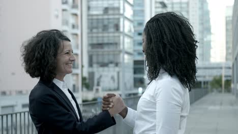 two laughing women shaking hands on street