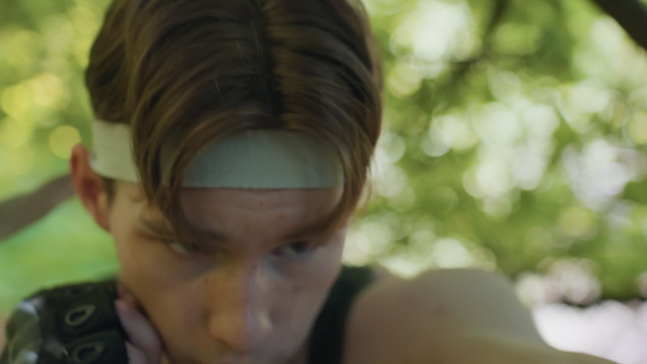 face view military man wearing headband throwing rapid punches while blocking opponent strike with one hand against blurred outdoor background conveying intense determined combat training session