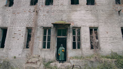 person in safety uniform alone in radiation zone. man in protective suit and gas mask with flowers near abandoned building after the chemical attack.
