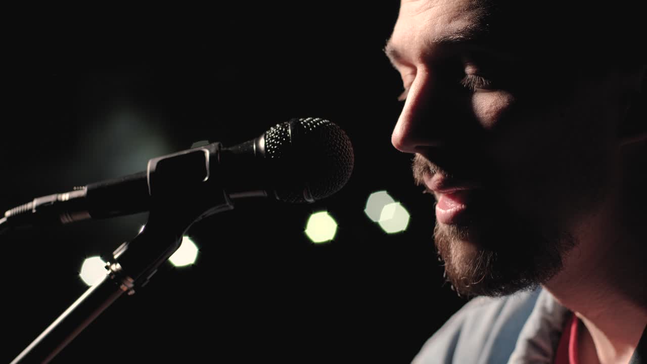 un músico está tocando la guitarra en un gran escenario con miembros de la audiencia sosteniendo linternas en el fondo. el auditorio está lleno de hermosas luces parpadeantes.