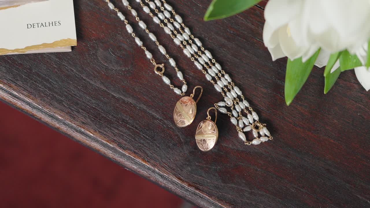 Rosary and engraved gold earrings rest on a wooden surface beside fresh tulips and a note