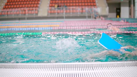 Young-boy-is-swimming-and-paddling-his-legs-inside-a-big-Olympic-size-pool