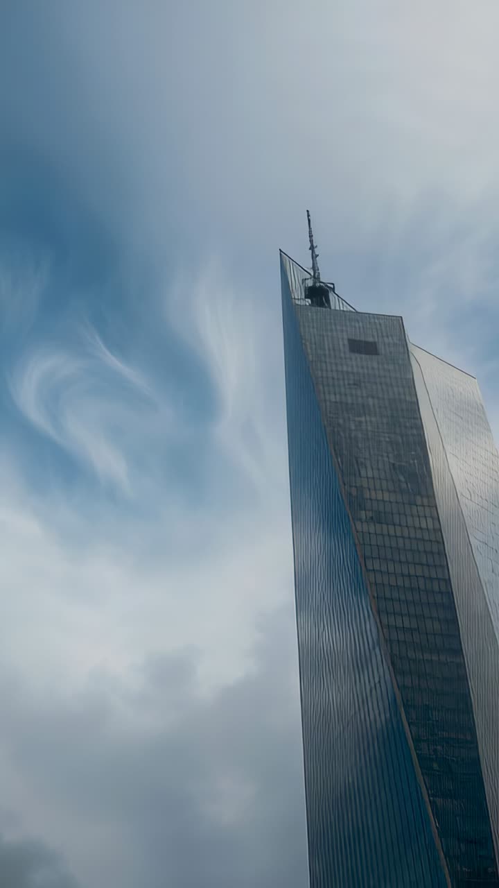 Video verticale: Torre di vetro con guglia e inquadratura bassa, che riflette le nuvole, spazio per il testo