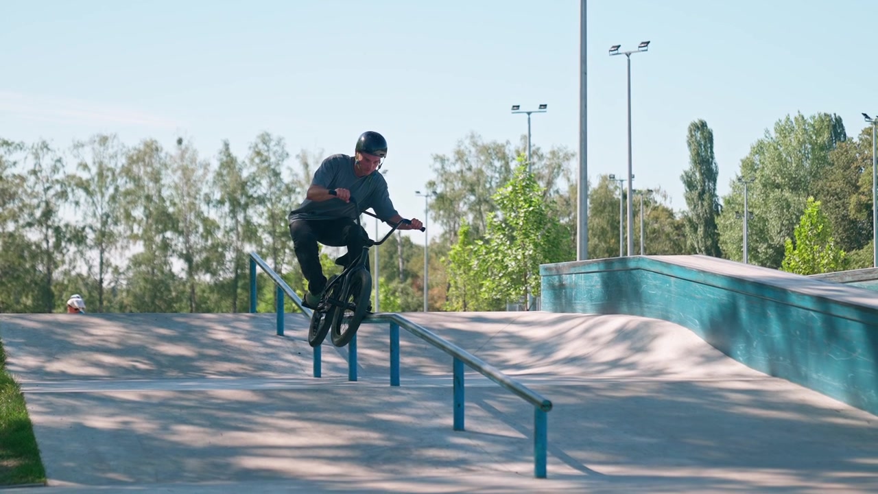 Młody mężczyzna wykonujący trick grind na BMX-ie na poręczy w skateparku