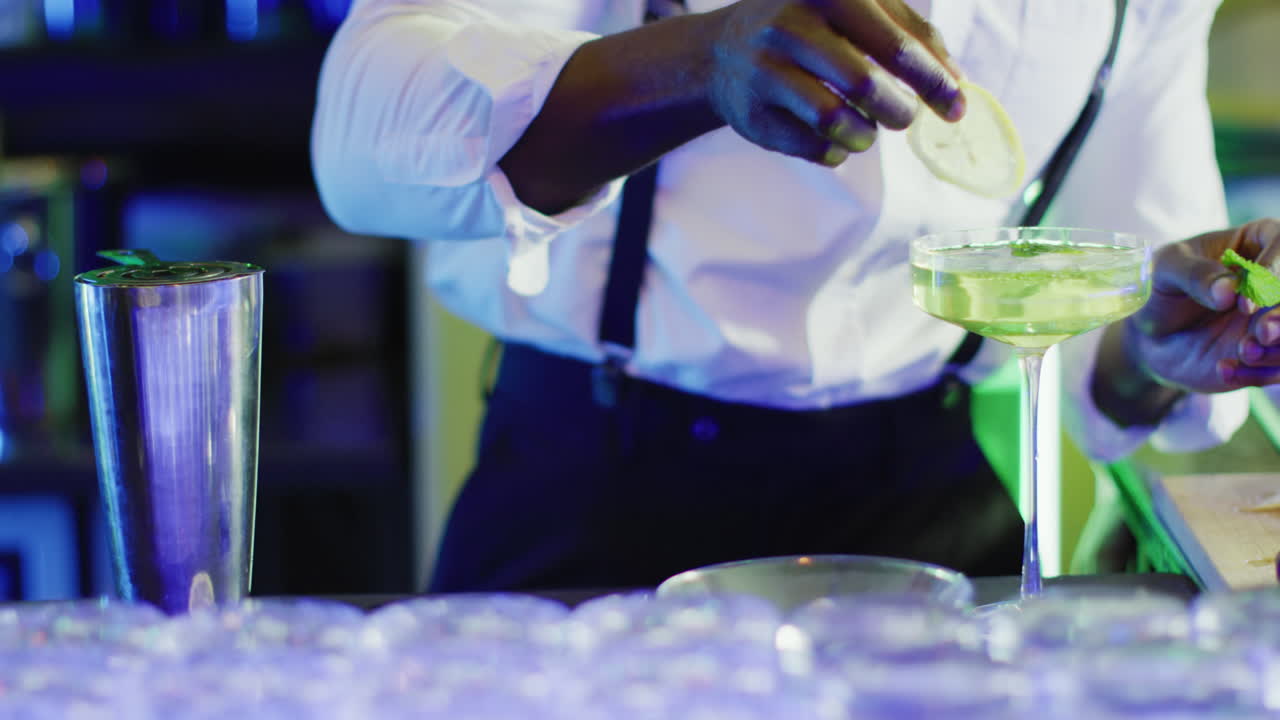 Video del busto di un barman afroamericano che prepara un cocktail verde al bar.