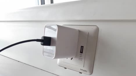 a hand plugs a usb charger into a wall socket, showing the connection process.