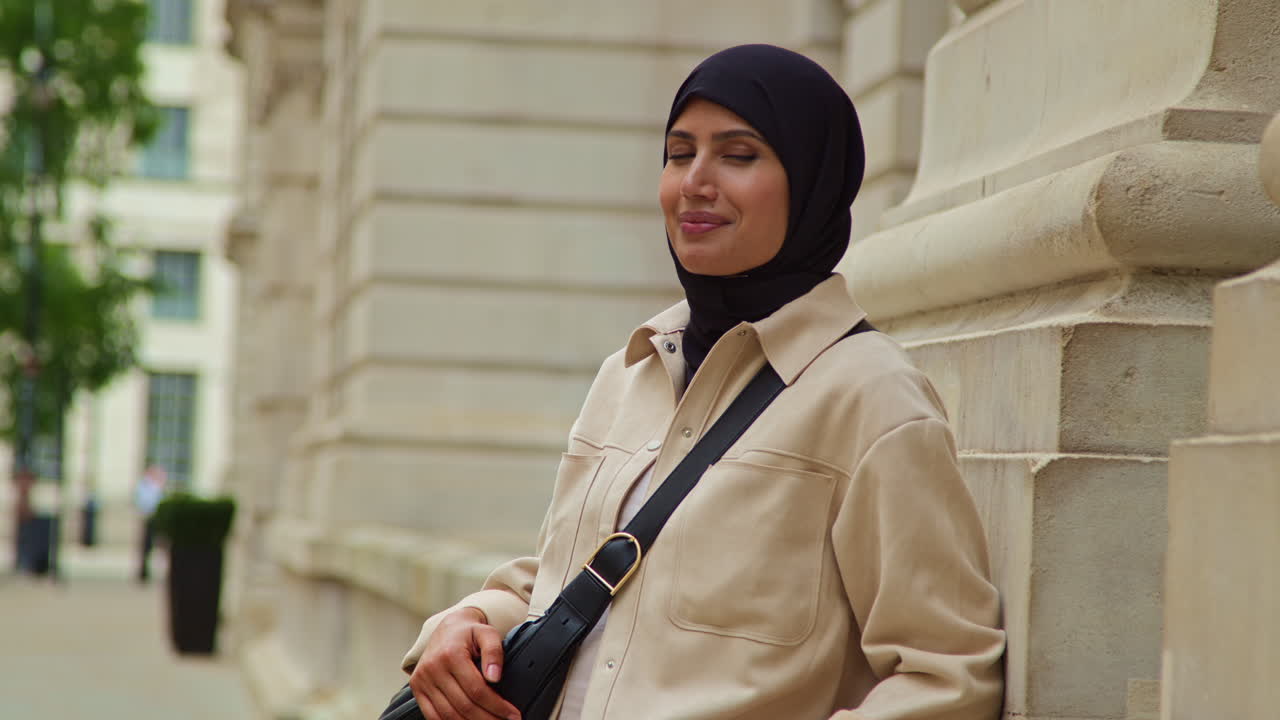 히자브를 입고 현대적인 비즈니스 슈트를 입은 웃는 무슬림 사업가 여성의 초상화 도시 사무실 건물 밖에서 서 있습니다.
