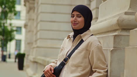 portrait of smiling muslim businesswoman wearing hijab and modern business suit standing outside city office buildings 3