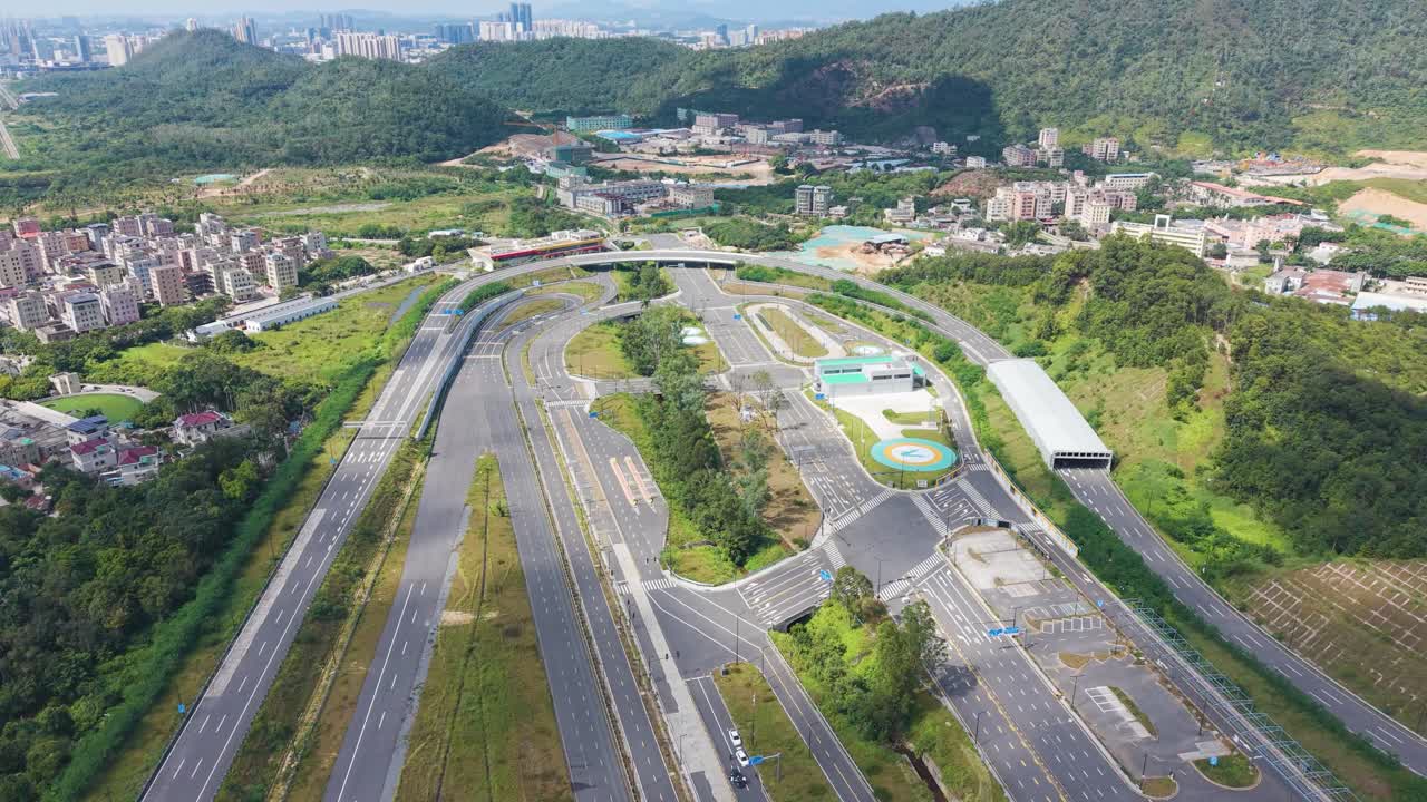 Aerial view of Shenzhen’s large vehicle testing facility with multiple road surfaces, lanes, and testing zones surrounded by green hills and urban areas. Automotive and infrastructure themes
