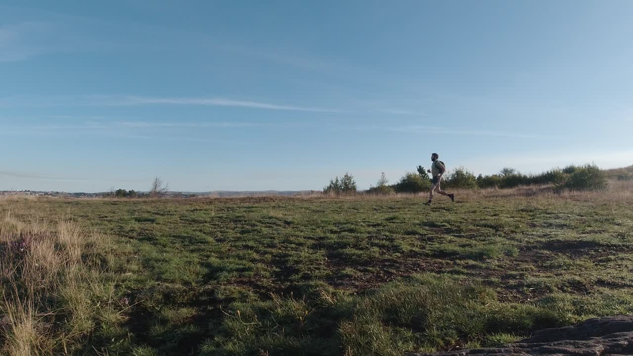 Grandangolo di un corridore che fa jogging attraverso un campo all'alba - Movimento lento.